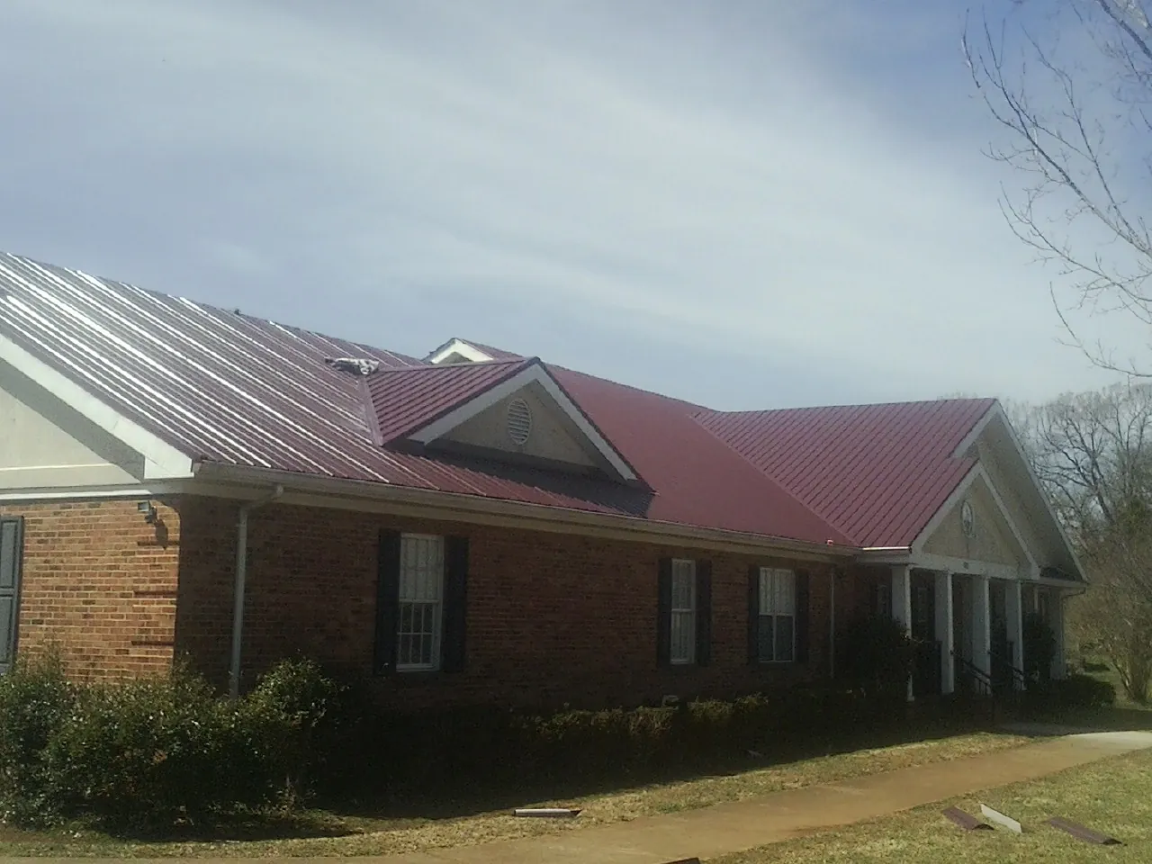 Red metal roof with gabled entries on a long brick building, from a Hail Damage Roof Repair job in Kirkville