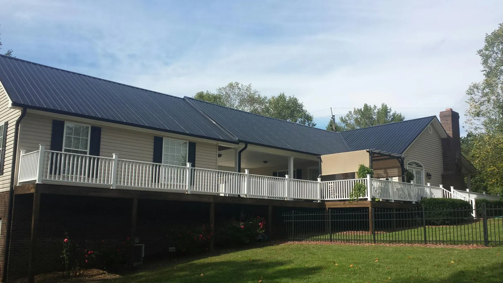 Black metal roof above a long white railed deck on a hillside home in Kirkville
