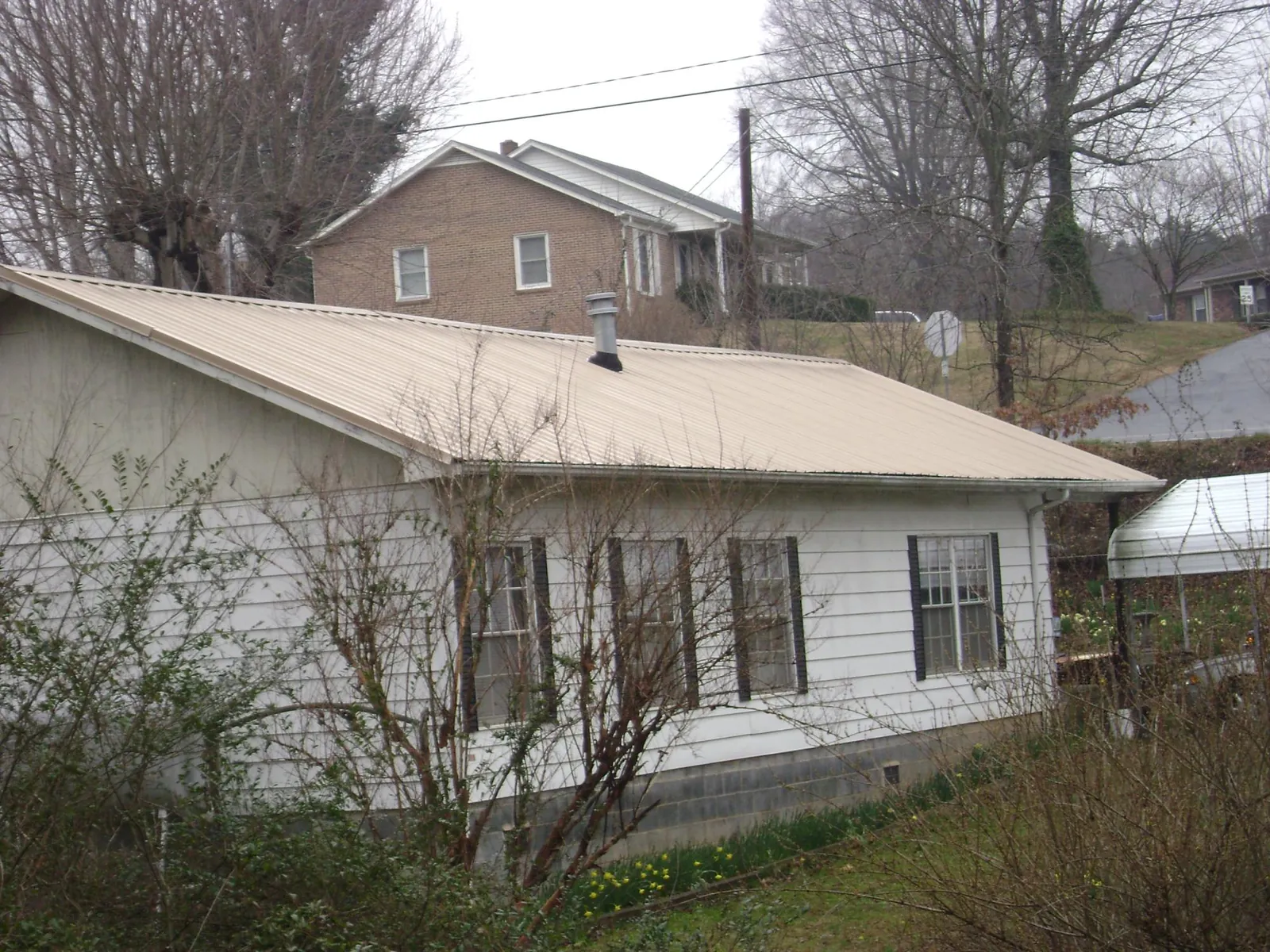 Tan metal roof on a white sided house set into a hillside — Commercial Roofing by Roofing Brothers in Kirkville
